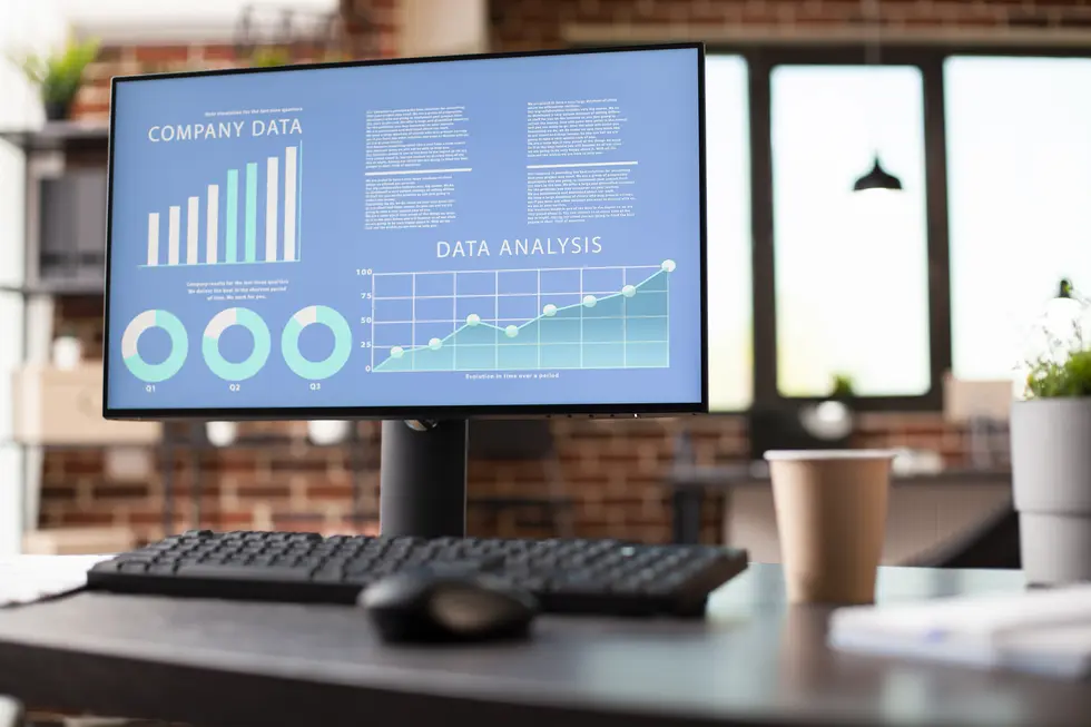 Datenanalyse-Dashboard auf einem Computerbildschirm mit Grafiken zu Unternehmensdaten, einschließlich Diagrammen und Auswertungen für die Quartale Q1 bis Q3, sowie einem Berichtstext zur Datenanalyse. Der Bildschirm ist auf einem Schreibtisch platziert, neben einer Kaffeetasse und einem Computerzubehör.
