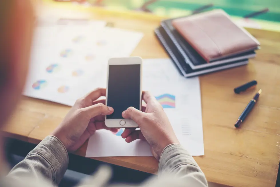 Person hält ein Smartphone in den Händen, während sie auf einem Tisch mit Dokumenten und Notizbüchern sitzen, die Diagramme und Grafiken zeigen.