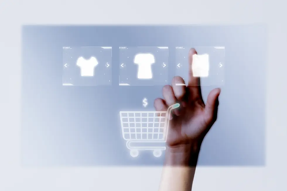 Interaktive Benutzeroberfläche für den E-Commerce, auf der eine Hand über digitale Produktbilder mit Shirts navigiert. Ein Einkaufswagensymbol und Preisschild sind sichtbar, was auf einen Online-Kaufprozess hinweist.