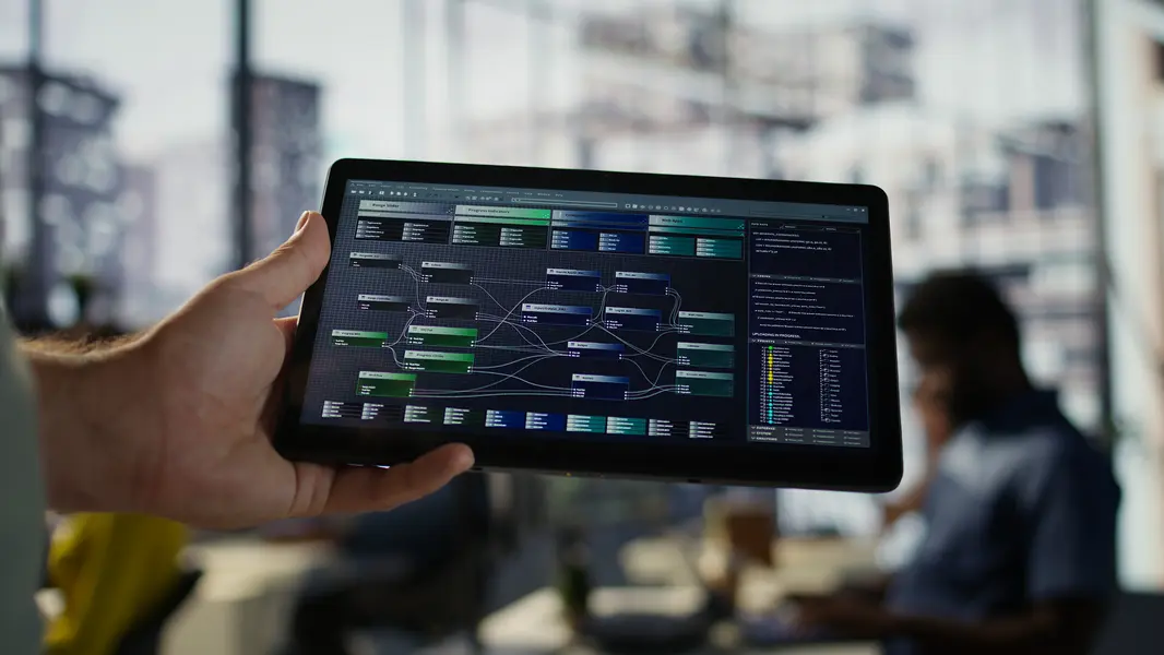 Hand, die ein Tablet hält, auf dem ein komplexes Datenvisualisierungsdiagramm mit verschiedenen Verbindungen und Kategorien dargestellt ist. Im Hintergrund sind schemenhafte Büroumgebungen und Menschen zu sehen, die an Computern arbeiten.