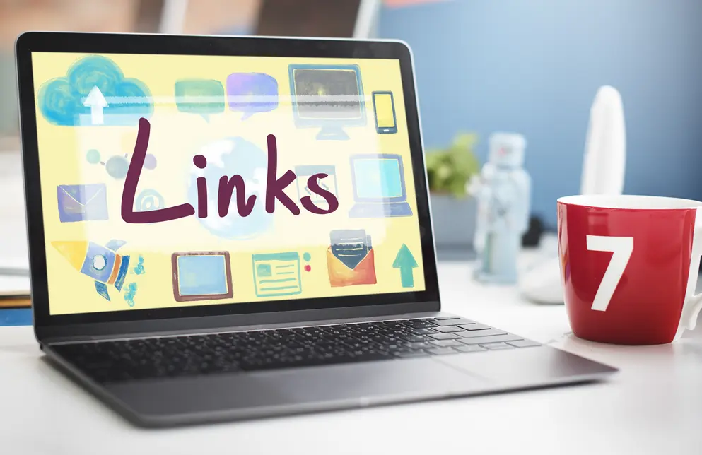 Laptop auf einem Tisch mit einer Grafik, die das Wort "Links" zeigt, umgeben von verschiedenen Symbolen wie Wolken, Computer und Pfeilen, ausgestattet mit einer roten Kaffeetasse mit der Zahl 7.