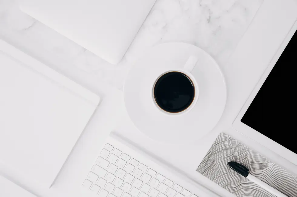 Moderne Arbeitsumgebung mit einem weißen Laptop, einem Notizbuch, einer Computertastatur, einer Kaffeetasse auf einem Unterteller und einem tablet, die alle auf einer Marmoroberfläche angeordnet sind. Ideal für digitale Arbeitsplätze und zur Verbesserung der Produktivität.