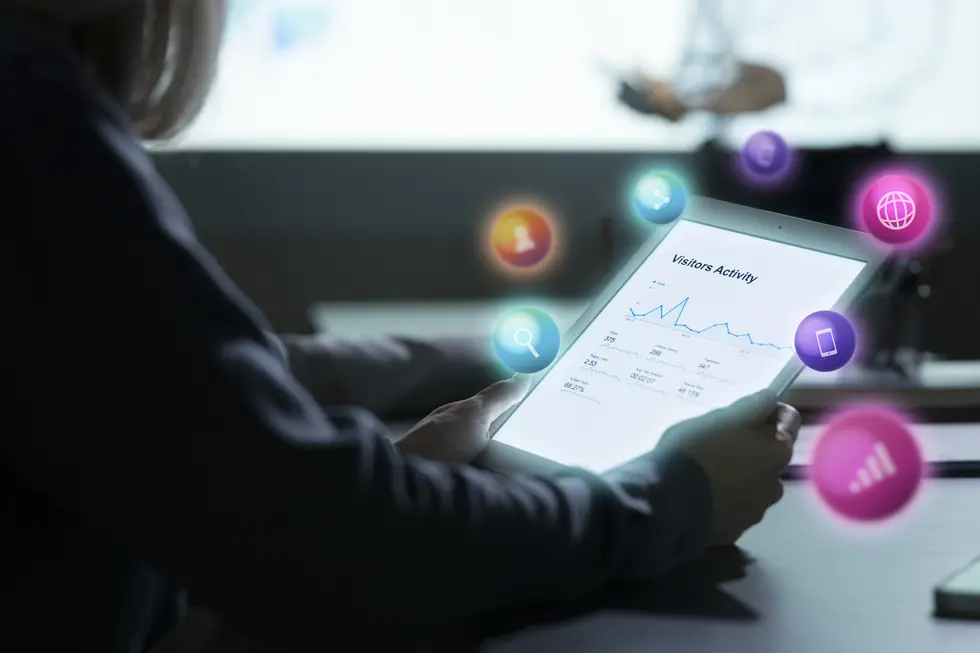 Tablet mit einer Analyse von Besucheraktivitäten und grafischen Darstellungen von Social Media Daten. Im Hintergrund scheinen verschiedene Icons zu schwebende, welche Funktionen wie Nutzerinteraktionen, Suchanfragen und Webaktivität symbolisieren. Das Bild vermittelt eine moderne Arbeitsumgebung, in der technologische Lösungen zur Analyse von Social Media eingesetzt werden.
