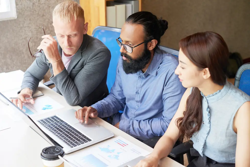 Teammeeting zur Analyse von Social Media Daten, bei dem drei Personen an einem Laptop arbeiten und verschiedene Dokumente mit Diagrammen und Grafiken studieren.