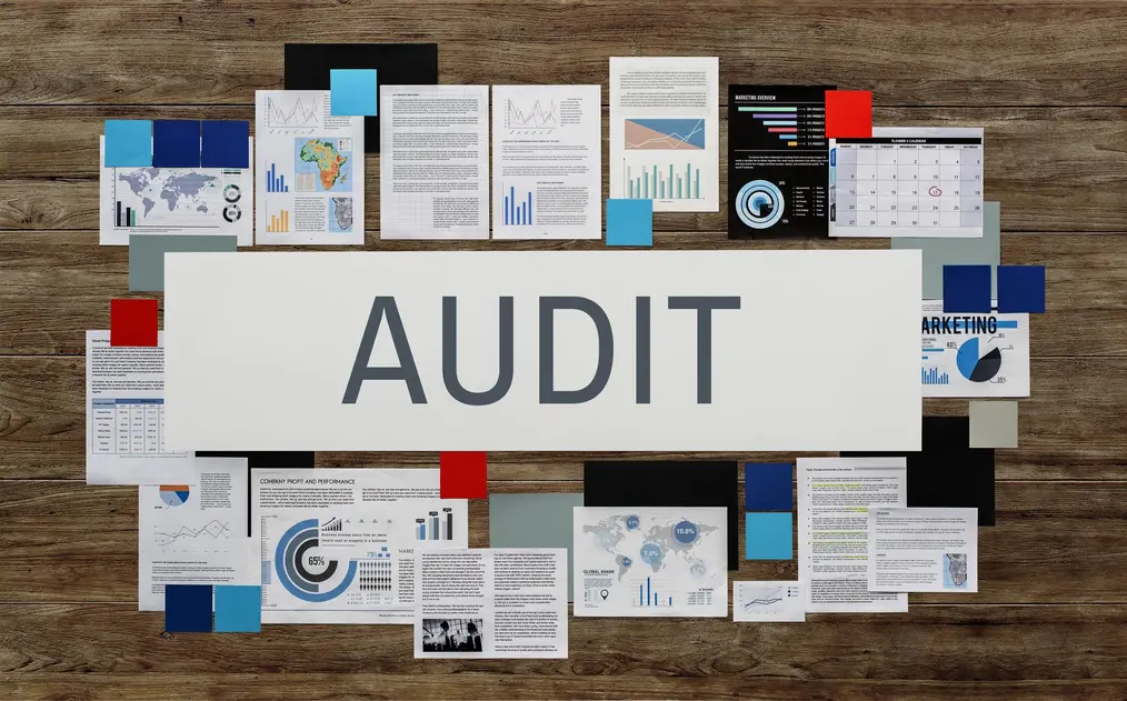Collage von Dokumenten und Grafiken zum Thema Audit, darunter Statistiken und Diagramme zur Analyse von Unternehmensdaten. Im Mittelpunkt steht der große Schriftzug "AUDIT", umgeben von verschiedenen Informationsblättern, die Marketing- und Performance-Daten darstellen, auf einem Holzuntergrund angeordnet.
