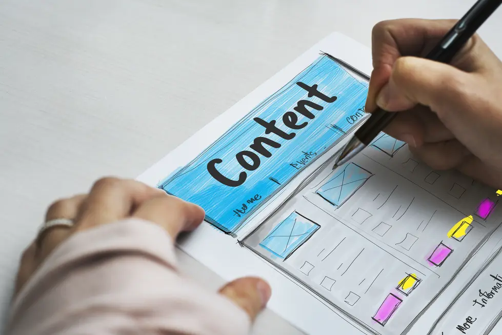 Hand, die einen Entwurf für eine Website zeichnet, mit dem Fokus auf das Wort "Content" in blauer Farbe. Der Entwurf zeigt verschiedene Bereiche für Inhalte, zum Beispiel Home, Events und Links, in einem skizzierten Layout auf Papier.