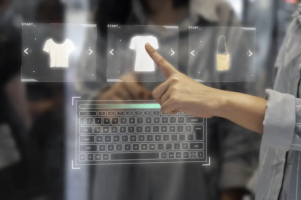 Finger einer Person interagiert mit einem holografischen Display, das virtuelle Kleidungsstücke und Handtaschen zeigt, während ein transparentes Keyboard im Vordergrund sichtbar ist. Das Bild vermittelt eine moderne Einkaufserfahrung im E-Commerce mit innovativen Technologien.
