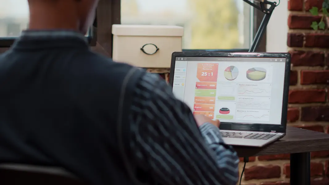 E-Commerce-Betreiber analysieren PPC-Kampagnen auf einem Laptop mit Business-Analytics-Dashboard, das Grafiken und Kennzahlen zur Umsatzprognose anzeigt, während sie an einem Tisch in einem modernen, lichtdurchfluteten Raum sitzen.