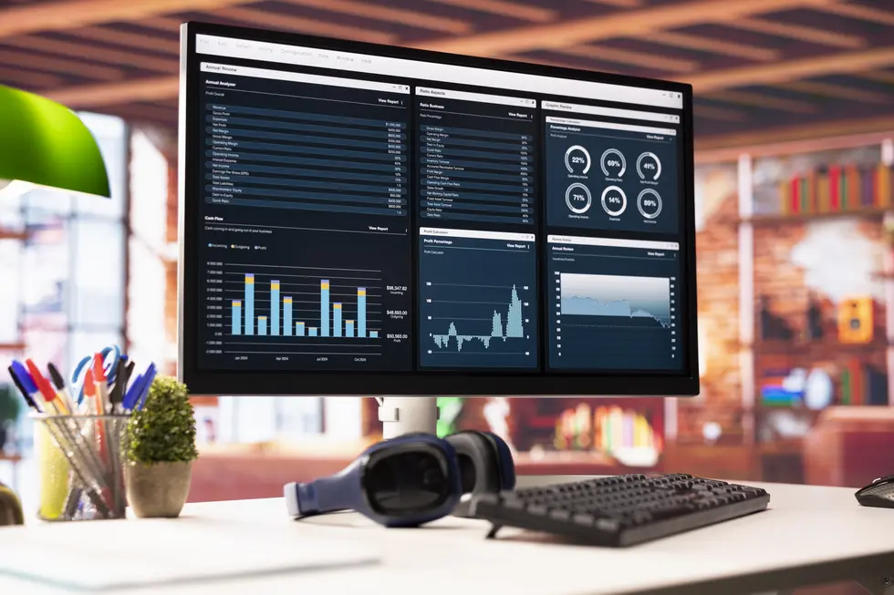 Überblicksdashboard mit integrierten Monitoring-Tools, das wichtige Kennzahlen und Analysen in einer modernen Büroumgebung darstellt. Auf dem Bildschirm sind grafische Auswertungen, Balkendiagramme und Leistungskennzahlen zu sehen, während eine Tastatur und Kopfhörer im Vordergrund für einen produktiven Arbeitsplatz stehen.