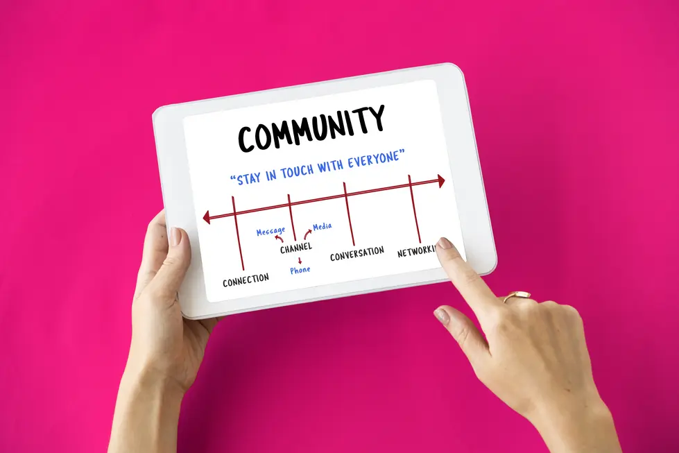 Person hält ein Tablet mit einer Grafik zum Thema "Community", die die Begriffe "Connection", "Channel", "Conversation" und "Networking" zeigt. Die Grafik vermittelt die Botschaft "Stay in Touch with Everyone" und betont die Wichtigkeit der verschiedenen Kommunikationskanäle. Der Hintergrund ist leuchtend rosa und hebt die Inhalte hervor.